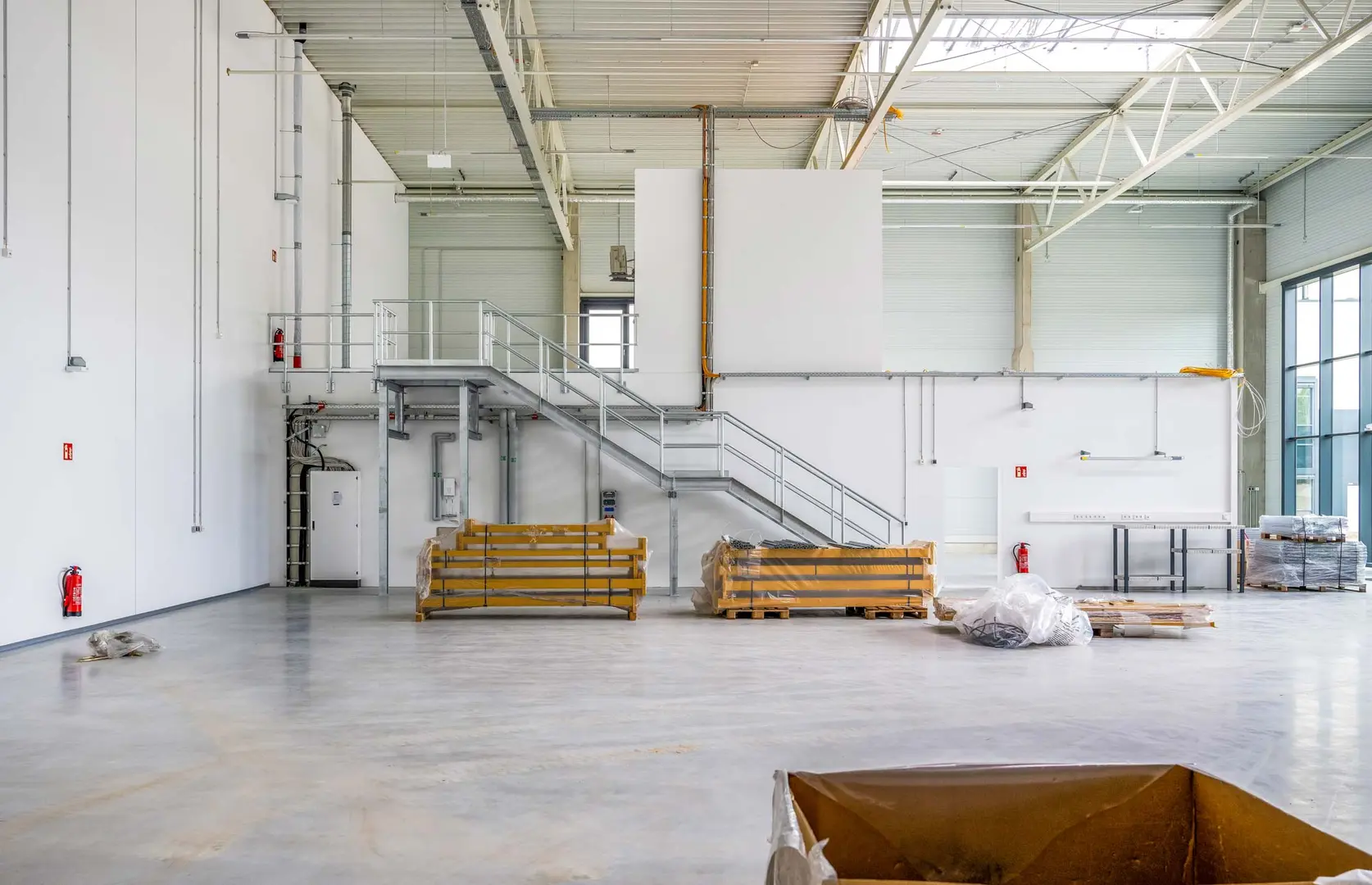 Fotografie aus dem Bauprozess des Spurwerkkomplexes. Dargestellt ist eine große Halle mit hohen Decken und einem Treppenaufgang zu einem offenen ersten Stock, auf dem Boden liegen Bauutensilien.