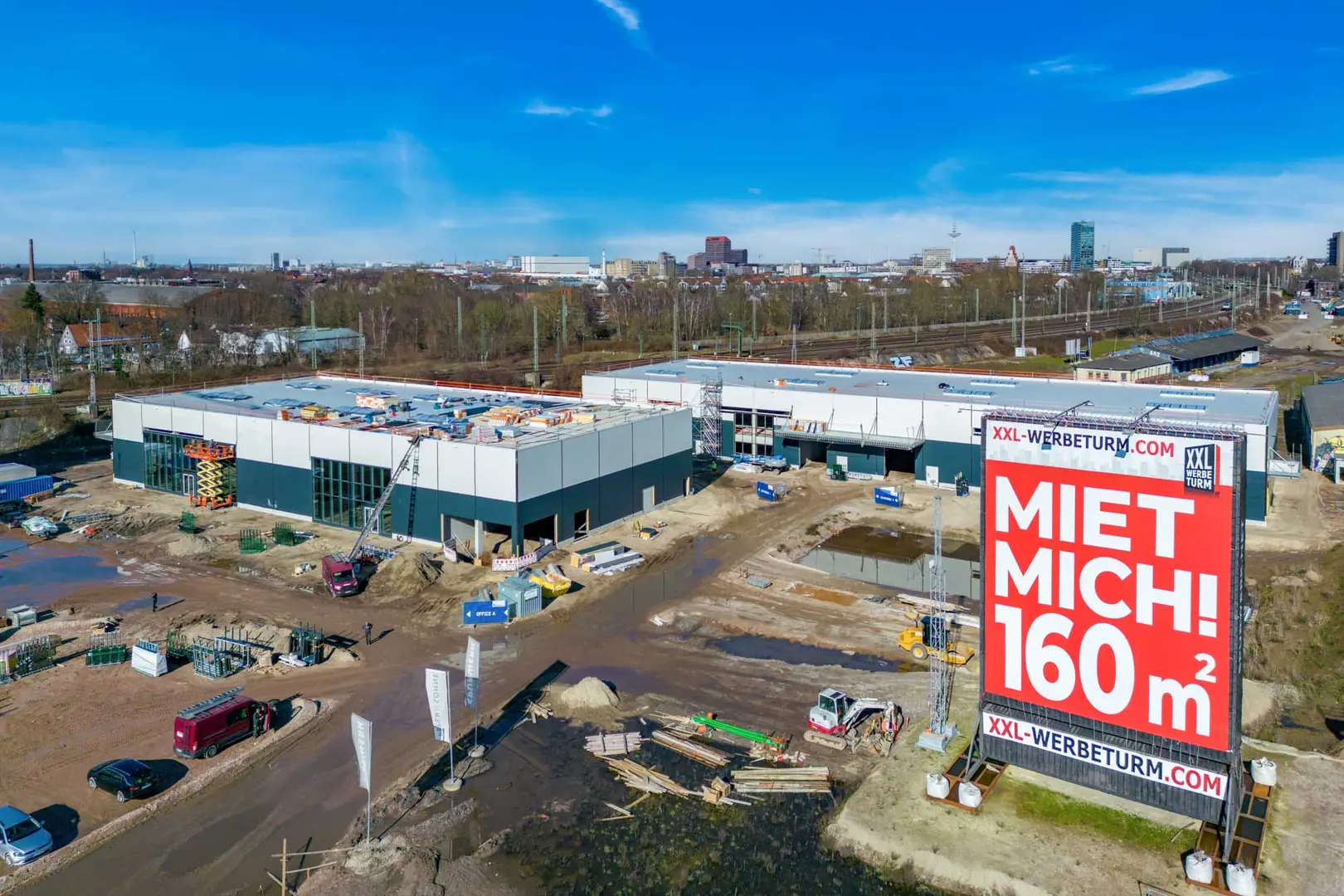 Foto aus der Bauphase des Spurwerkkomplexes. Abgebildet sind zwei Gebäude mit mehreren Baufahrzeugen davor.