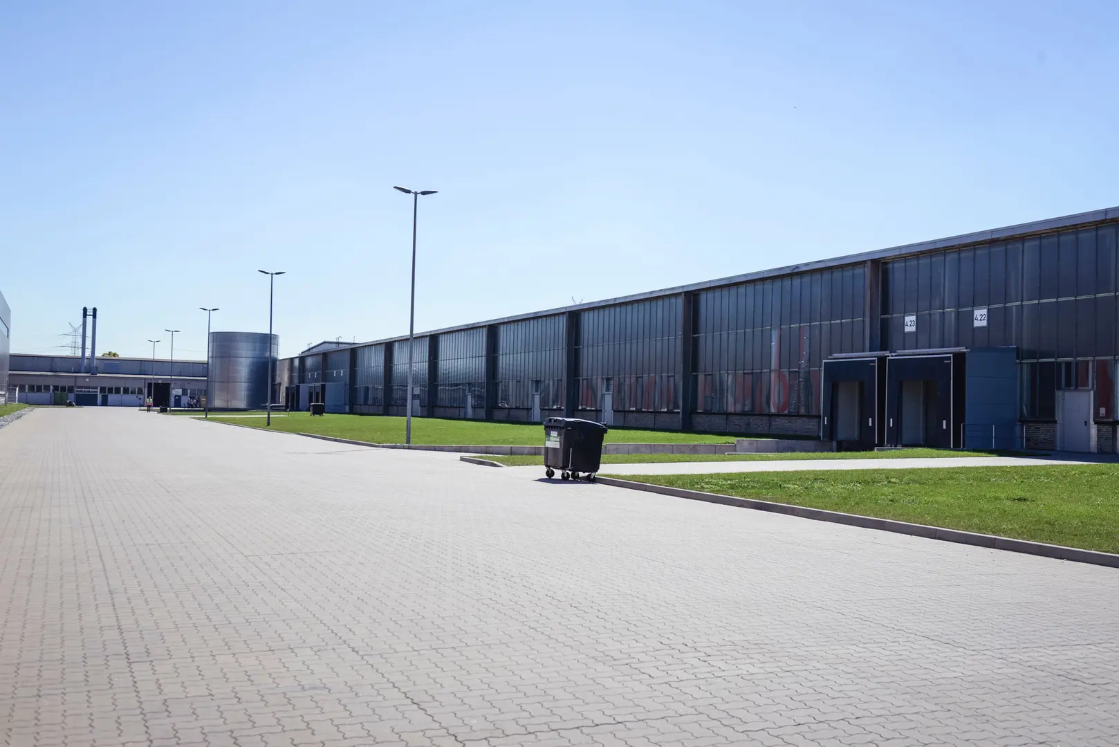 Foto einer Lagerhalle. Abgebildet ist eine sehr lange Lagerhalle mit dunkler Fensterfront und Verladestationen für LKW.